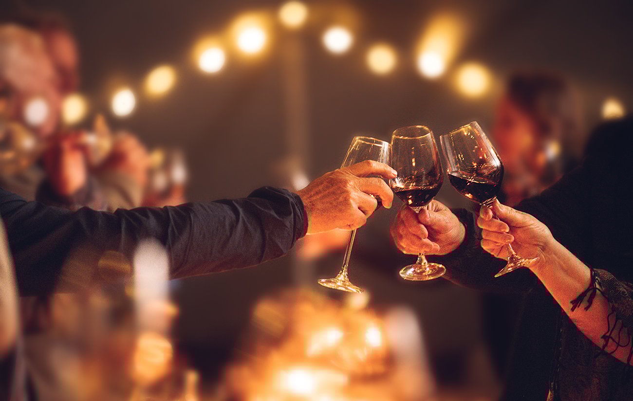 Celebratory red wine toast between senior adult friends at candle light social event party with string fairy lights iStock-1397143960